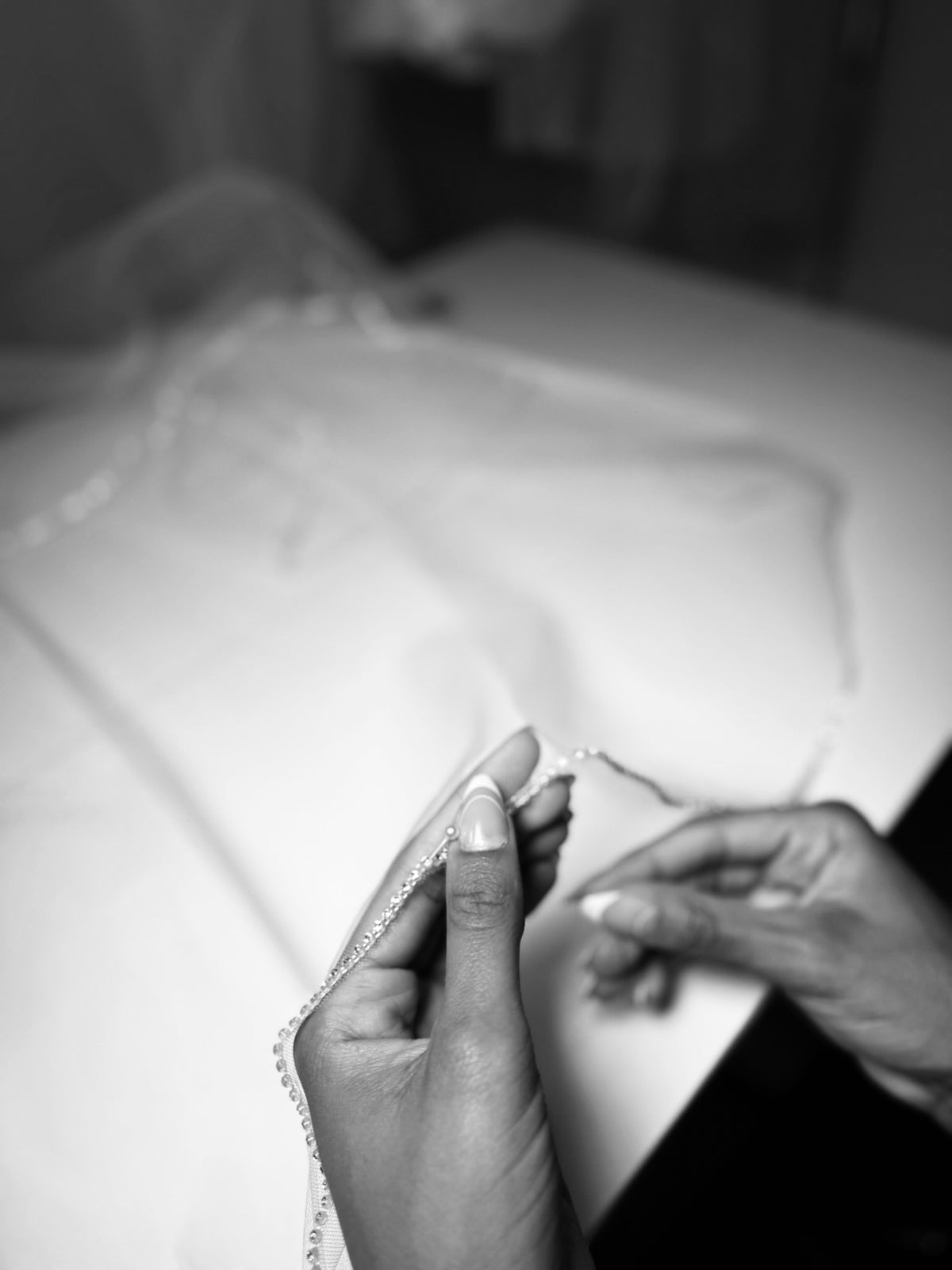 Close-up of hands with a focus on an artisan sewing a crystal wedding veil trim.